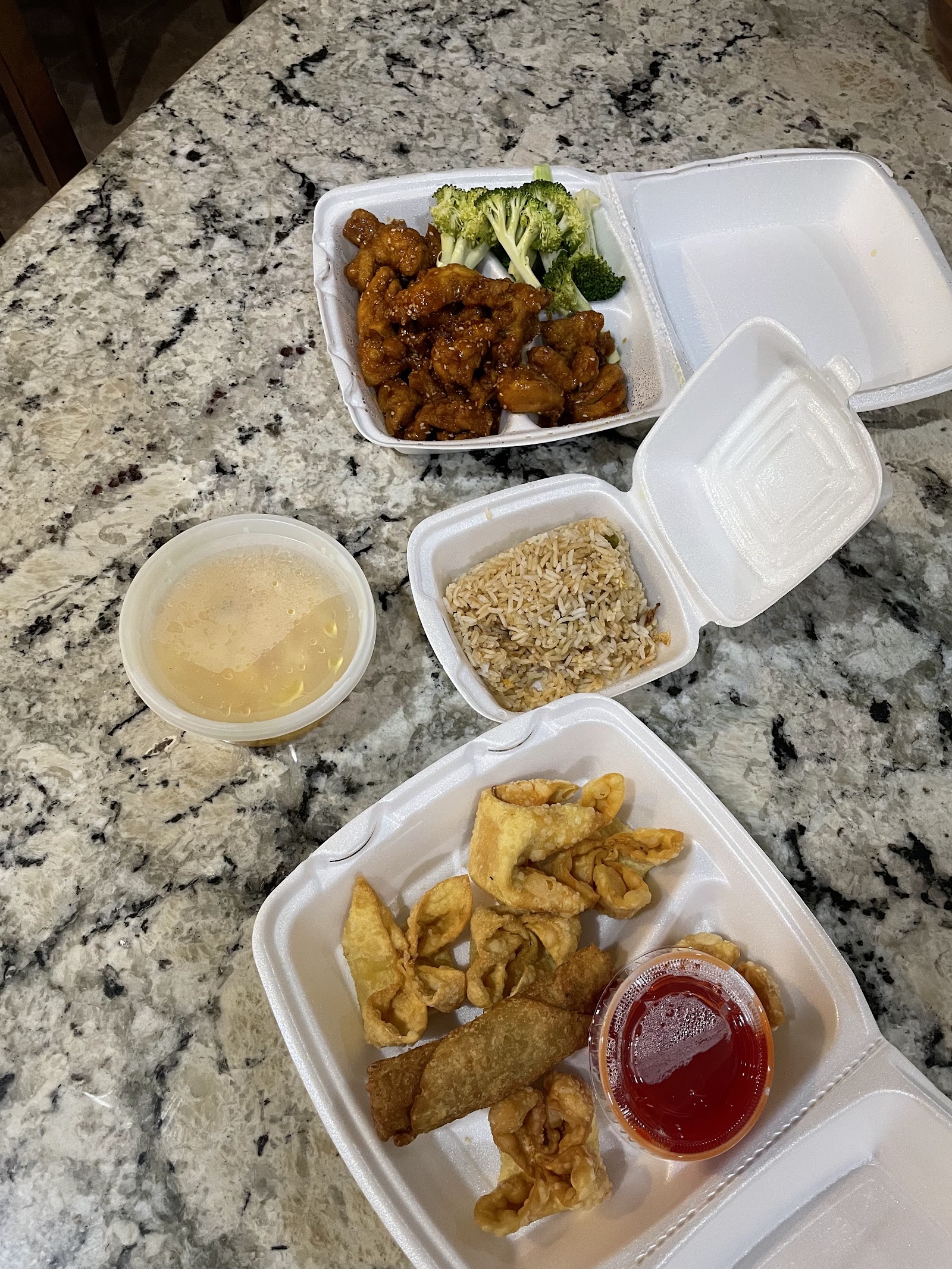 To-go containers of sesame chicken, fried rice, and fried wontons